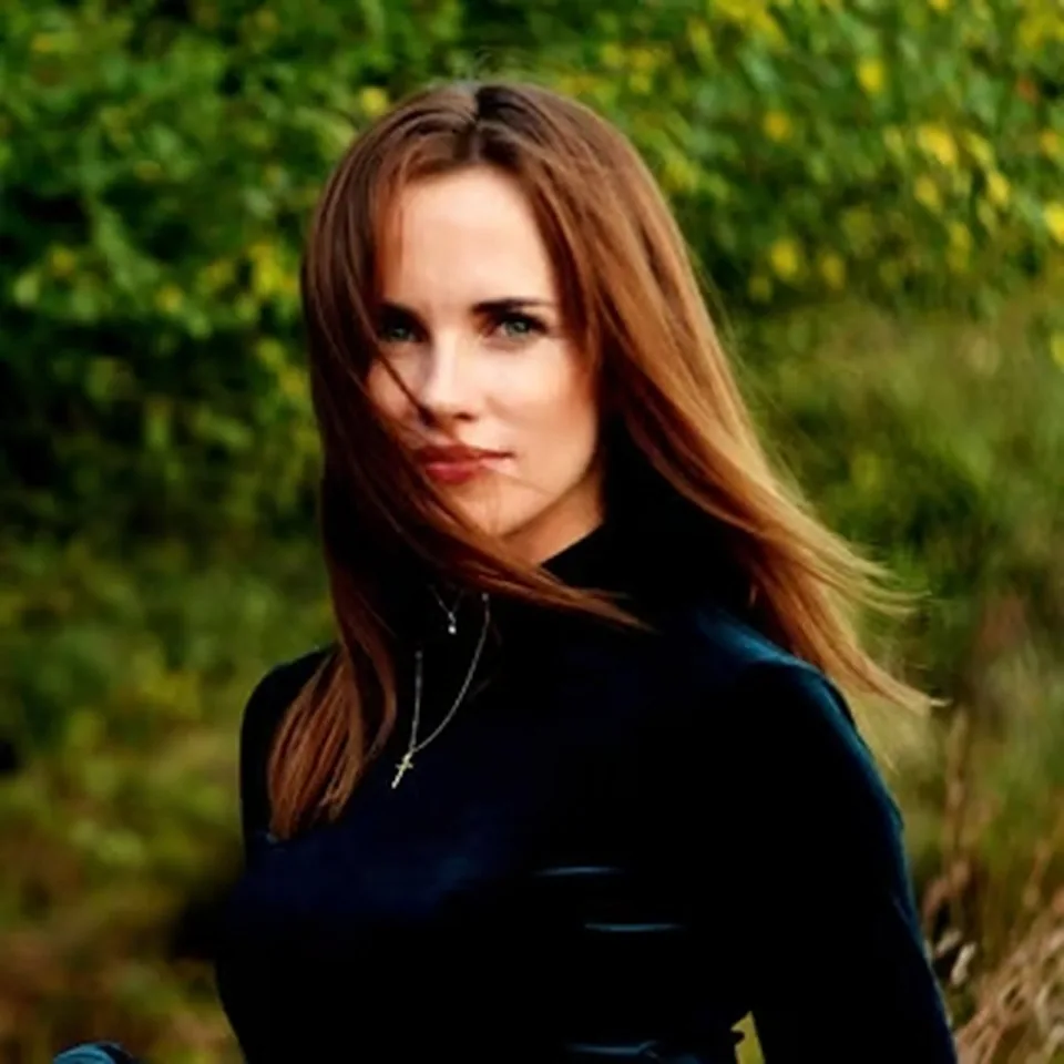 Portrait of Nataliia Ivaniv, with long auburn hair, in a dark velvet top, outdoors among greenery